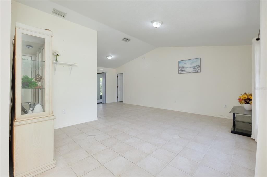 A spacious living room features light-colored tile flooring, vaulted ceilings, and a white display cabinet — 23235 MCQUEENEY AVENUE, PUNTA GORDA, FL