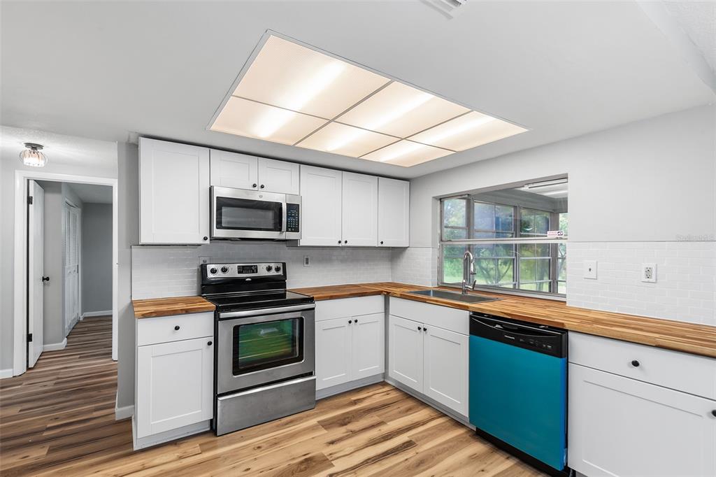 A kitchen features white cabinets, butcher block countertops, stainless steel appliances, and wood-look flooring — 7913 RAINTREE DRIVE, NEW PORT RICHEY, FL