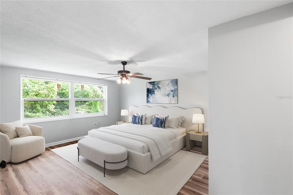 A bedroom features a king-sized bed, a ceiling fan, and a chair on wood flooring — 7913 RAINTREE DRIVE, NEW PORT RICHEY, FL