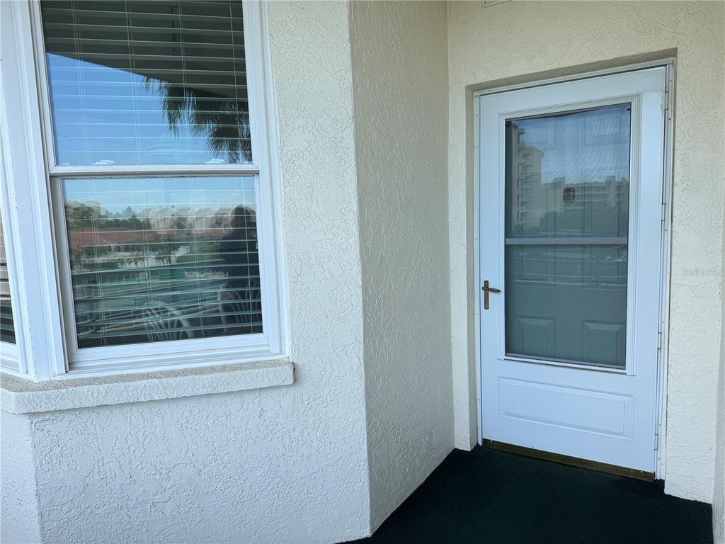 A white exterior wall features a window with blinds next to a white storm door — 7979 SAILBOAT KEY BOULEVARD S UNIT 306, SOUTH PASADENA, FL