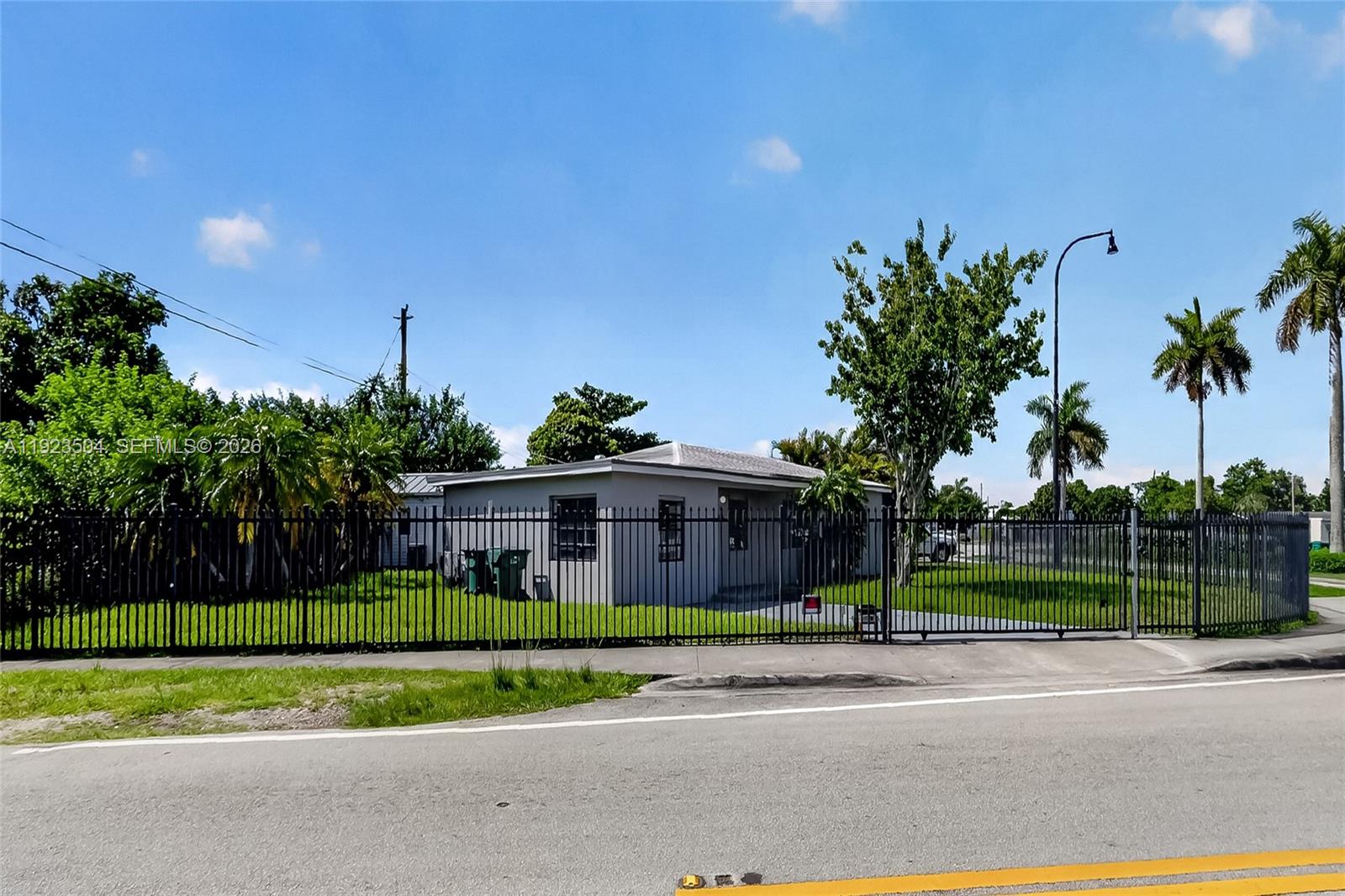 A gray single-story house sits behind a black metal fence on a grassy lot — 14801 Lincoln Blvd, Miami FL 33176, MIAMI, FL
