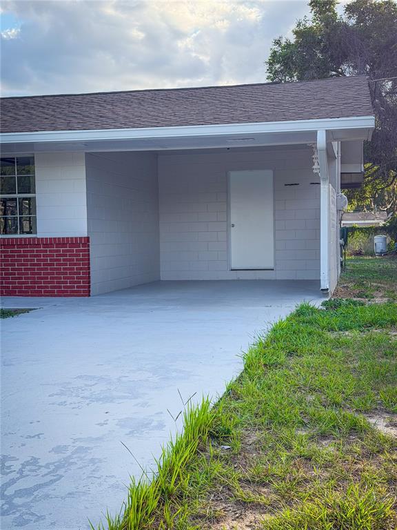 A concrete driveway leads to a covered carport with a white door and brick accents — 2104 SW 38TH AVENUE, OCALA, FL