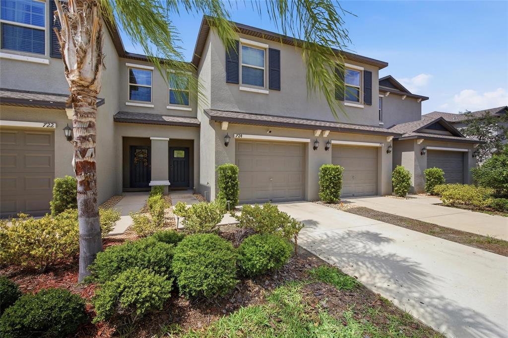 A row of multi-story townhomes with beige stucco facades, attached garages, and manicured landscaping — 724 ROYAL EMPRESS DRIVE, RUSKIN, FL