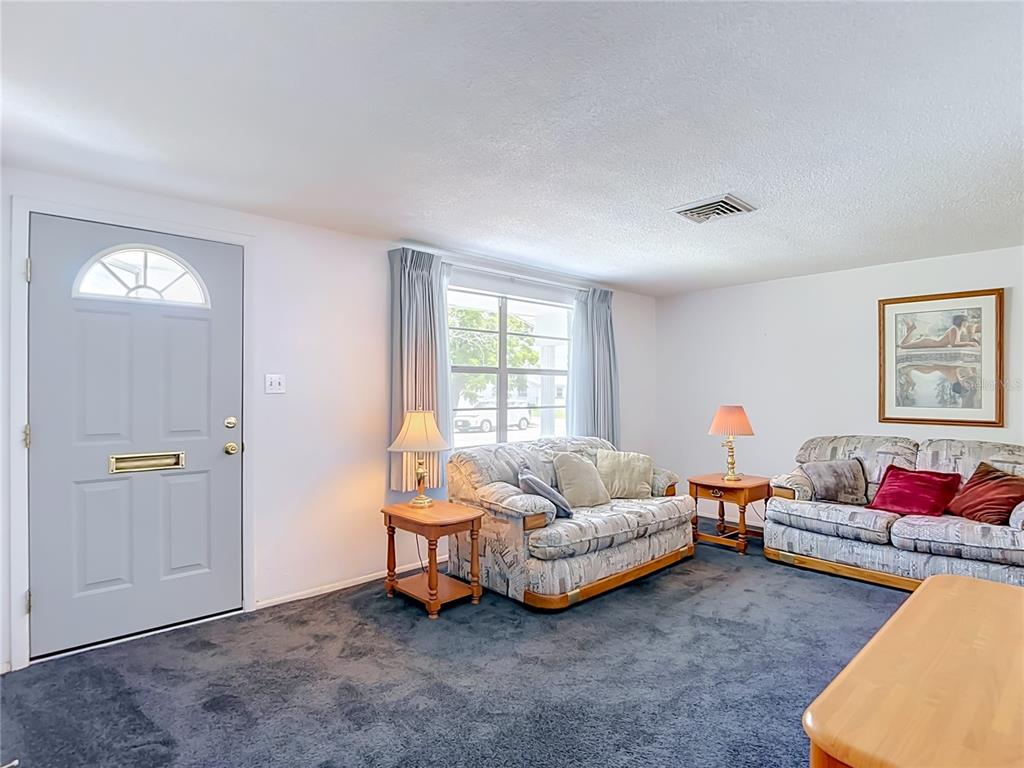 A living room features dark blue carpeting, two patterned sofas, and a light blue door — 4617 CROTON DRIVE, NEW PORT RICHEY, FL