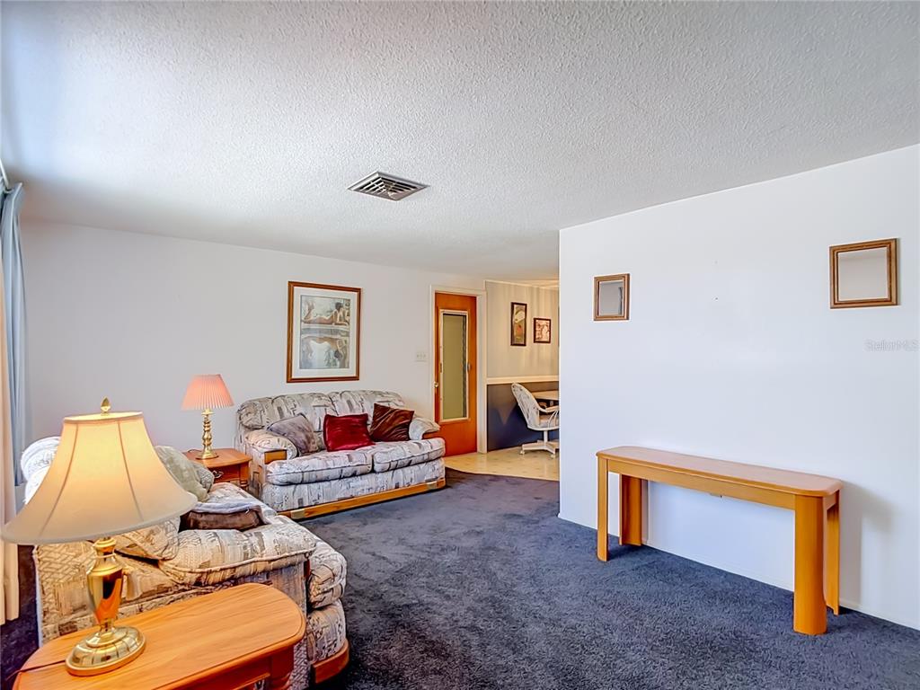 A living room features dark carpeting, two patterned sofas, a console table, and a doorway — 4617 CROTON DRIVE, NEW PORT RICHEY, FL