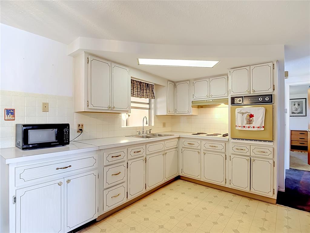 A kitchen with white cabinets, a wall oven, a double sink, and light-colored vinyl flooring — 4617 CROTON DRIVE, NEW PORT RICHEY, FL