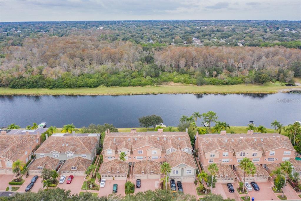 An aerial view shows townhomes with tile roofs situated along a river and wooded area — 1626 LAGO VISTA BOULEVARD, PALM HARBOR, FL