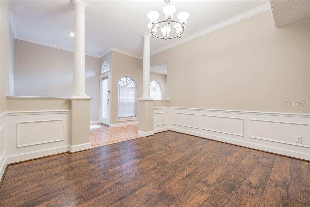 A dining room features wood-look flooring, white wainscoting, two decorative columns, and a chandelier — 1626 LAGO VISTA BOULEVARD, PALM HARBOR, FL