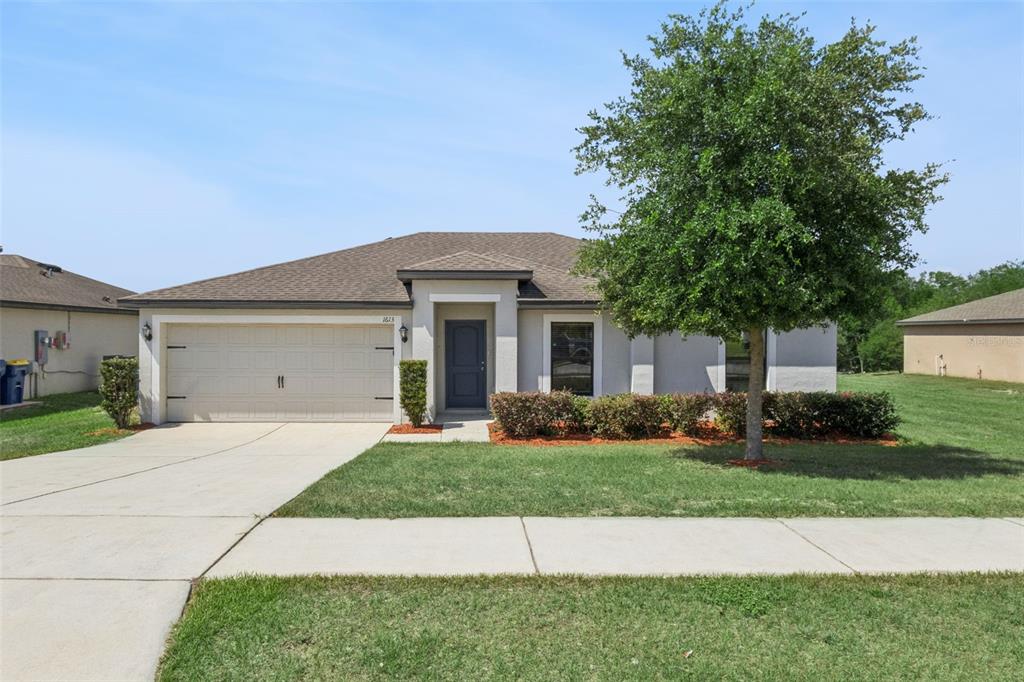 A single-story house with a beige exterior, a two-car garage, and a large front tree — 1613 ORNE STREET, MASCOTTE, FL