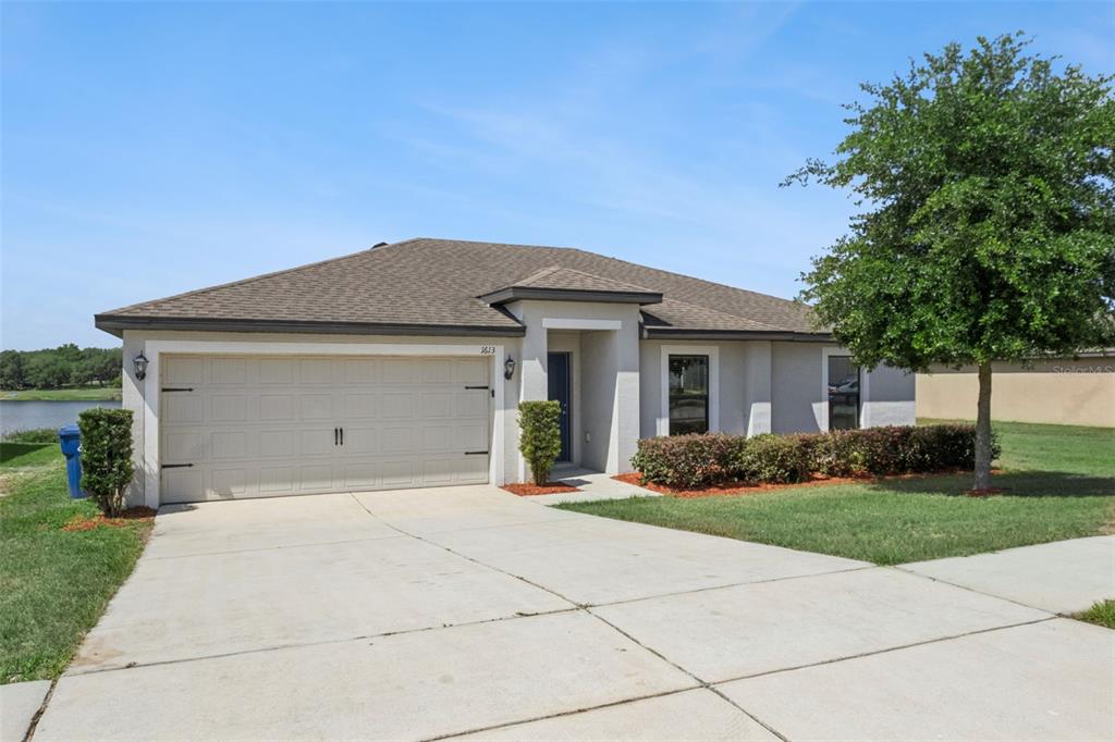 A single-story house with a beige stucco exterior, a two-car garage, and a concrete driveway — 1613 ORNE STREET, MASCOTTE, FL