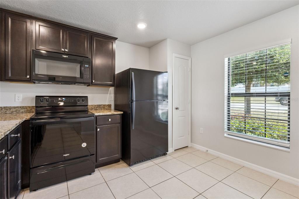 A kitchen features dark wood cabinets, black appliances, granite countertops, and a window with blinds — 1613 ORNE STREET, MASCOTTE, FL