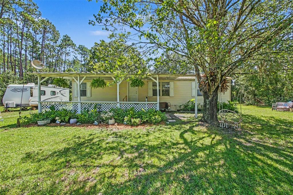 A single-story manufactured home with a covered front porch sits on a grassy, wooded lot — 2375 GROVE STREET, BUNNELL, FL