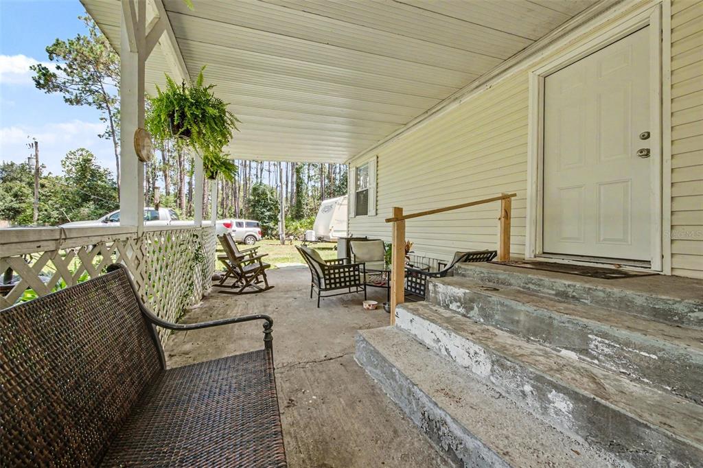 A covered concrete porch features a white door, steps, and outdoor furniture — 2375 GROVE STREET, BUNNELL, FL