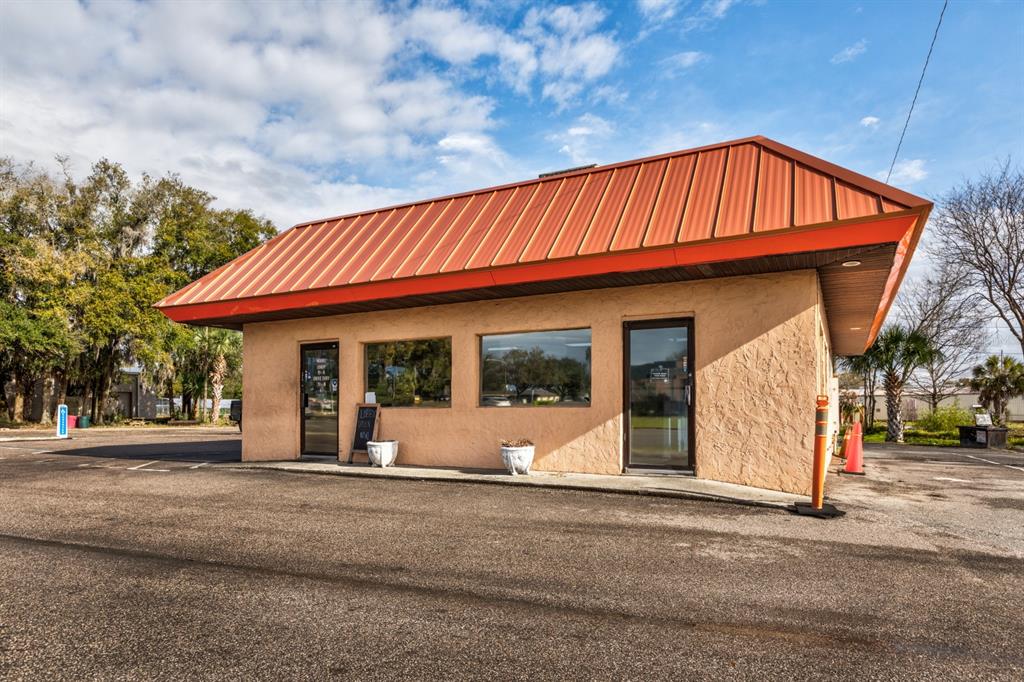 A single-story commercial building with a tan stucco exterior and a red metal roof — 299 E BROAD STREET, GROVELAND, FL