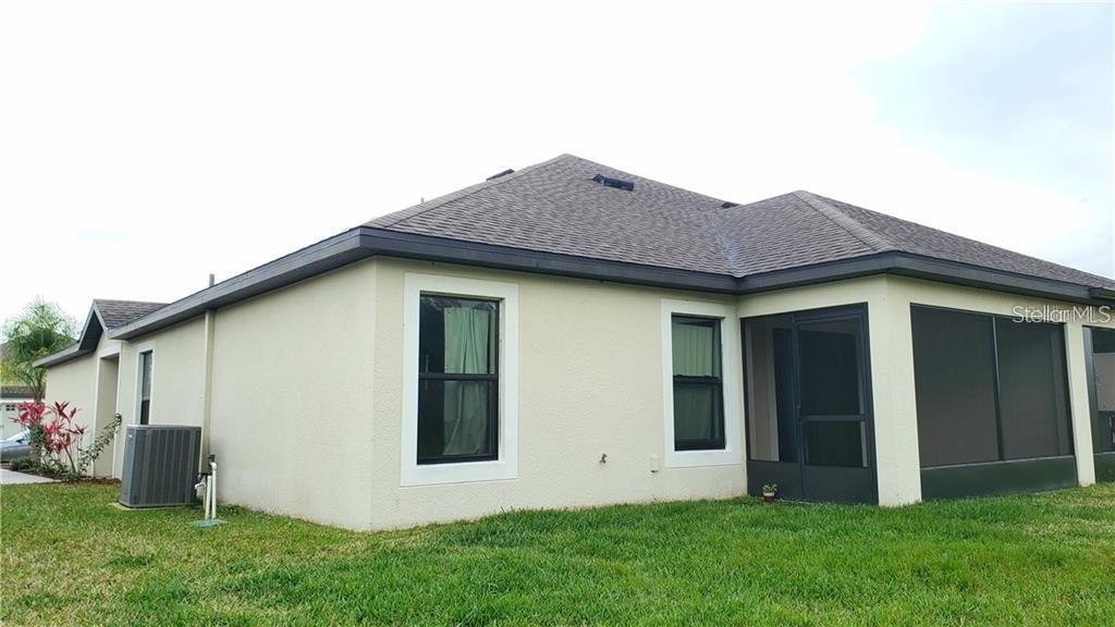 The exterior of a beige house features a screened-in porch and a central air unit — 5578 MAGGIORE BOULEVARD, LAKELAND, FL