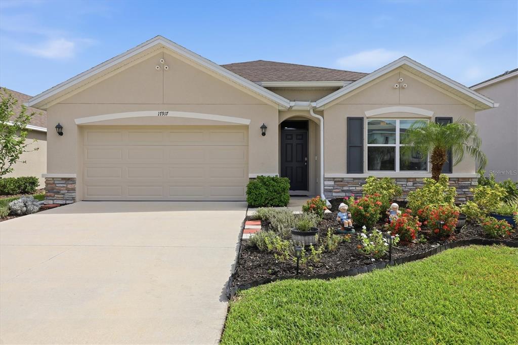A single-story suburban house with a beige stucco exterior, a two-car garage, and landscaping — 17917 CANOPY PLACE, BRADENTON, FL