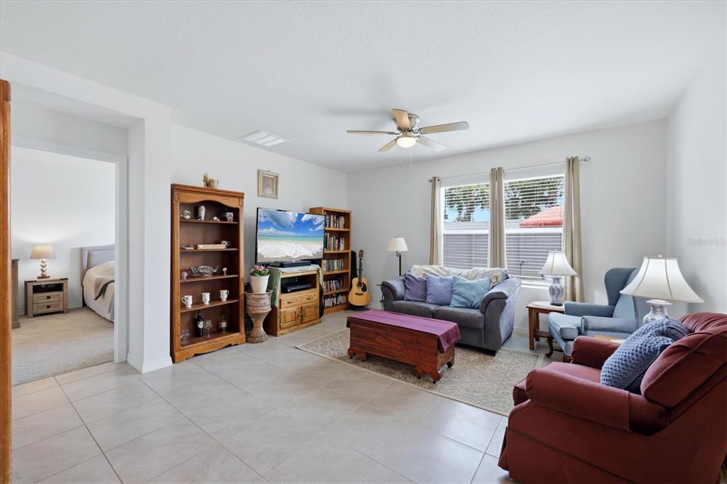 A living room features tile flooring, a ceiling fan, bookshelves, and a television — 17917 CANOPY PLACE, BRADENTON, FL