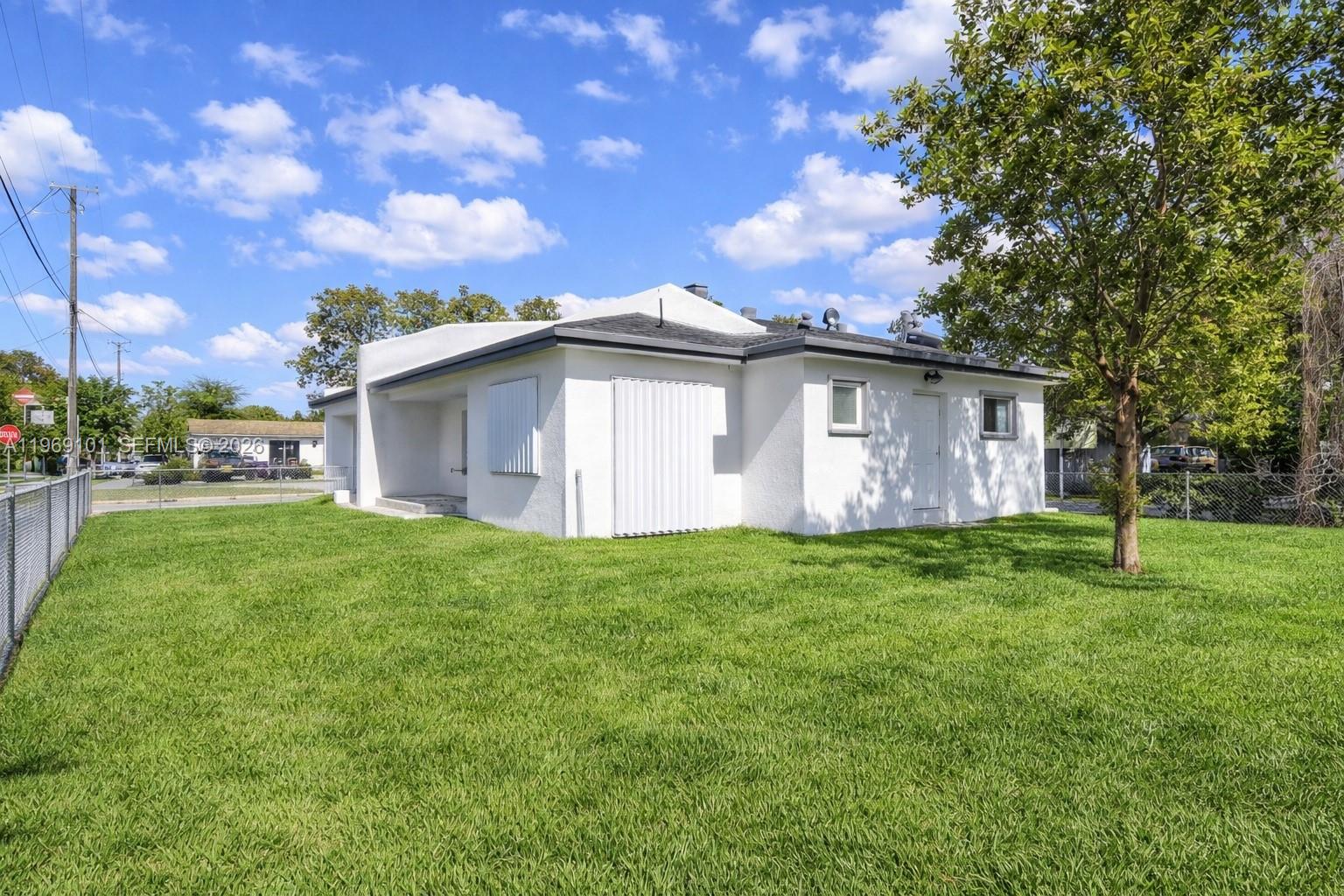 A white, single-story house with a fenced yard and hurricane shutters under a blue sky — 1998 NW 47th St, Miami FL 33142, MIAMI, FL