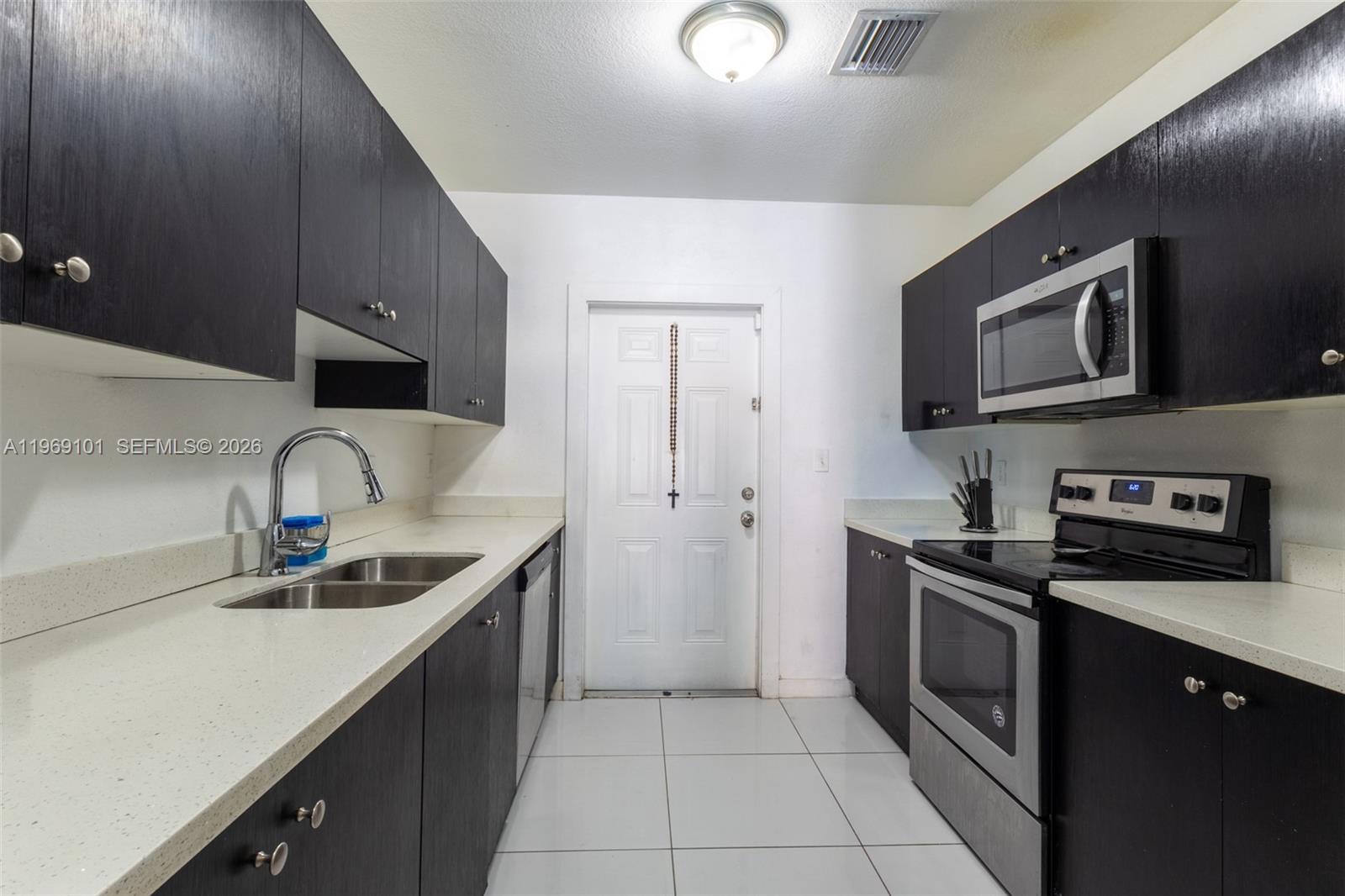 A galley kitchen features dark wood cabinets, light countertops, stainless steel appliances, and white tile flooring — 1998 NW 47th St, Miami FL 33142, MIAMI, FL