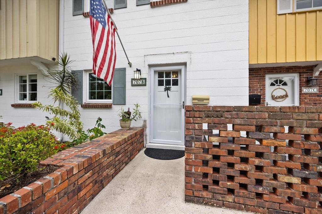 The exterior of a townhouse features a white facade, a brick wall, and an American flag — 707 W VENICE AVENUE UNIT 707B, VENICE, FL