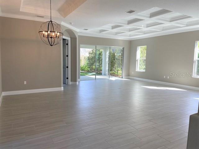 A spacious room features light-colored tile flooring, a coffered ceiling, and a modern chandelier — 7 OASIS CIRCLE, PALM COAST, FL