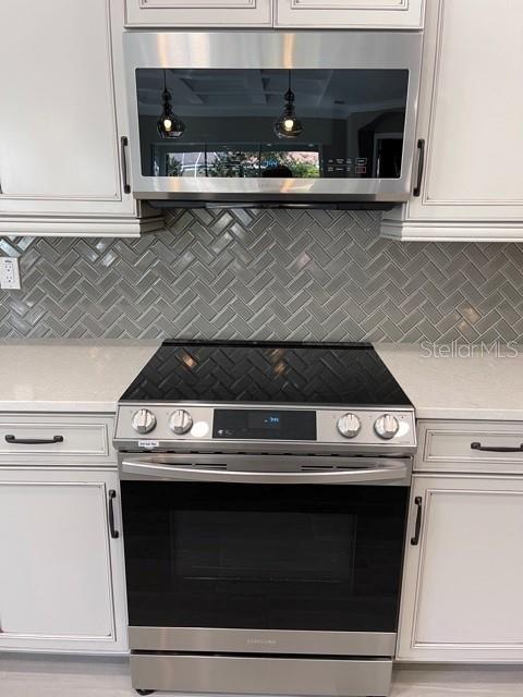 A stainless steel range and microwave are set against a gray herringbone tile backsplash — 7 OASIS CIRCLE, PALM COAST, FL