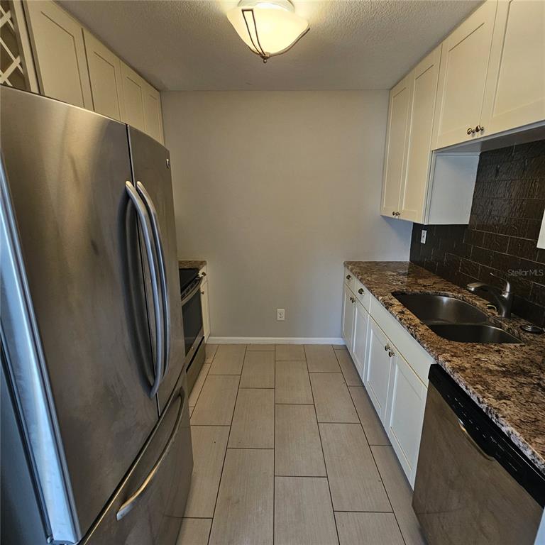 A galley kitchen features white cabinets, granite countertops, stainless steel appliances, and light tile flooring — 1902 DANDRIDGE STREET UNIT 12, SUN CITY CENTER, FL