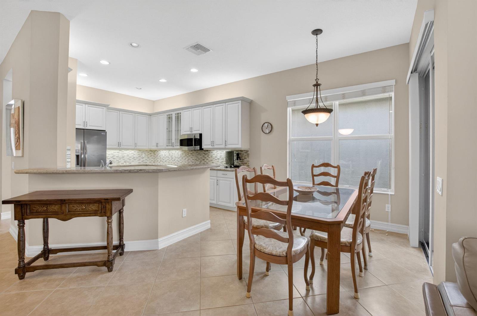 A kitchen with white cabinets and granite countertops opens to a dining area with tile floors — 9052 Greenstone Ridge Way, Boynton Beach FL 33473, BOYNTON BEACH, FL