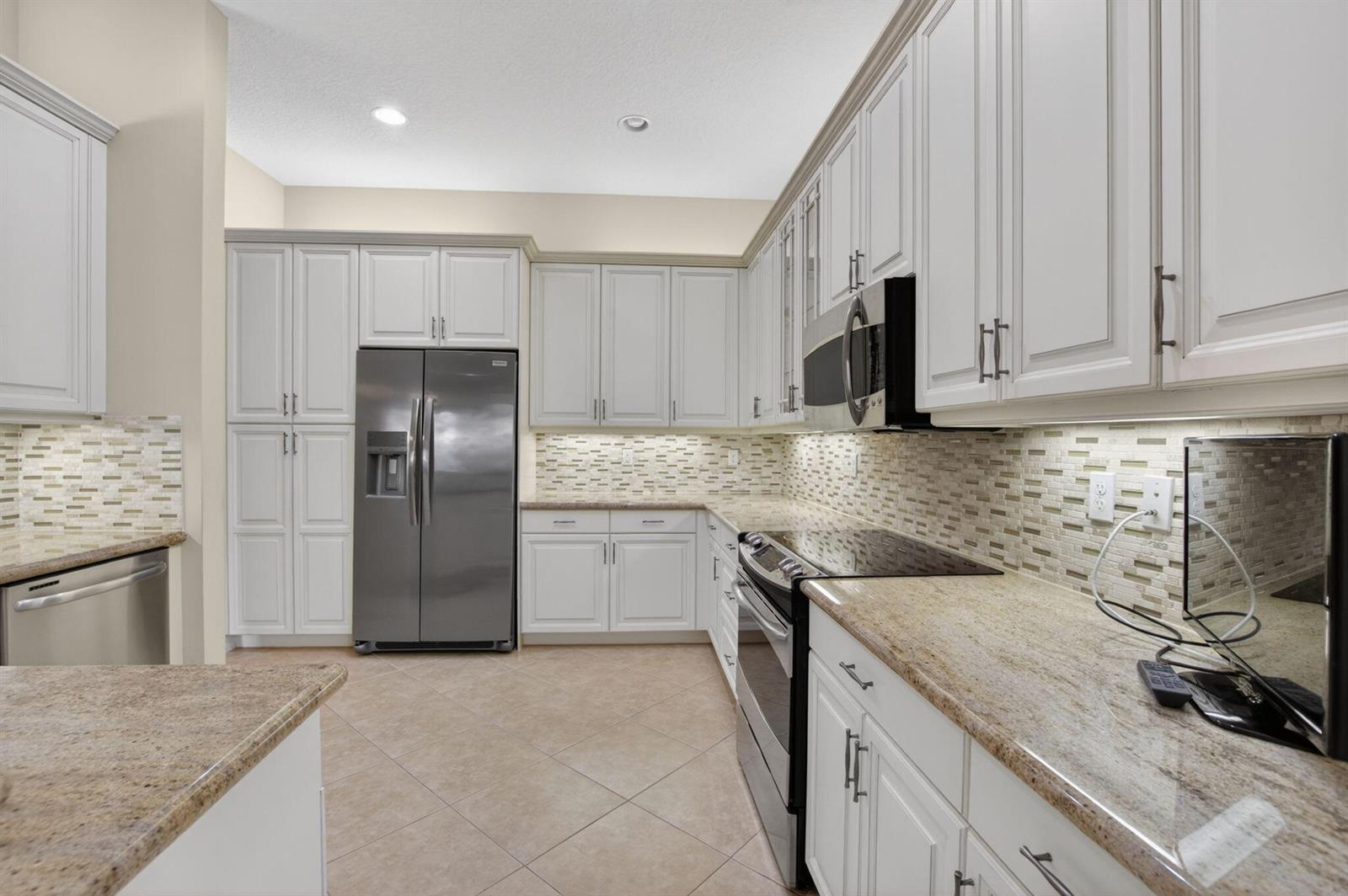 A kitchen features white cabinetry, granite countertops, stainless steel appliances, and a tiled backsplash — 9052 Greenstone Ridge Way, Boynton Beach FL 33473, BOYNTON BEACH, FL