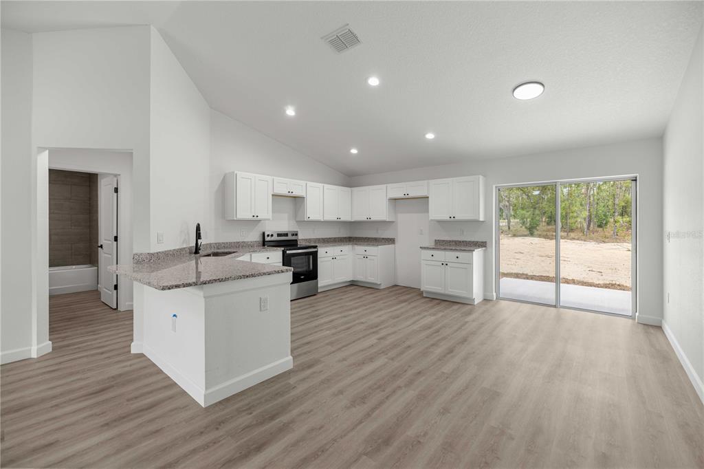 A kitchen with white cabinets, granite countertops, and light wood-look flooring opens to a patio — 24013 NW TAMARIND LANE, DUNNELLON, FL