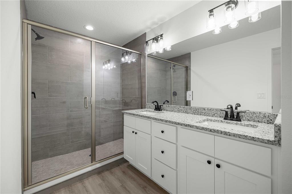 A bathroom features a double vanity with granite countertops, white cabinets, and a glass-enclosed shower — 24013 NW TAMARIND LANE, DUNNELLON, FL