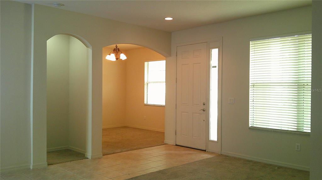An interior view shows a tiled entryway, a carpeted room with an arched opening, and a front door — 609 CEDAR WAXWING DRIVE, BRANDON, FL