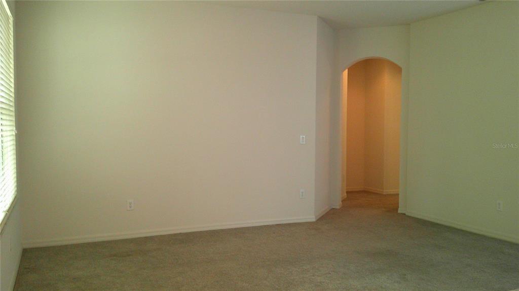 An empty room with beige carpet, light-colored walls, and an arched doorway leading to another area — 609 CEDAR WAXWING DRIVE, BRANDON, FL