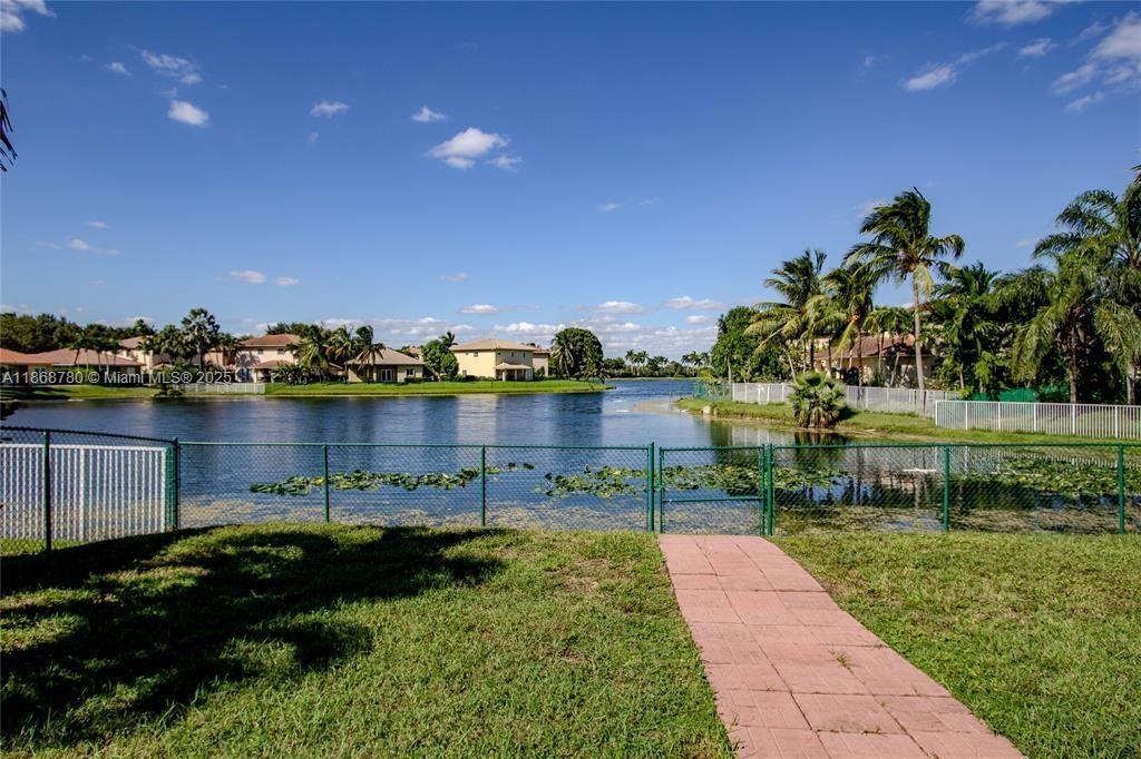 A paved walkway leads to a fenced lakefront area with palm trees and residential houses — 14129 SW 31st St, Miramar FL 33027, MIRAMAR, FL