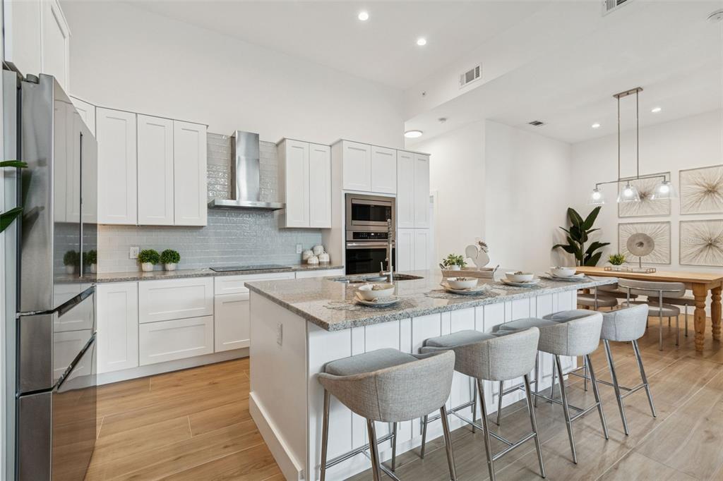 A modern kitchen features white cabinets, granite countertops, a central island, and stainless steel appliances — 1343 4TH STREET UNIT 102, SARASOTA, FL
