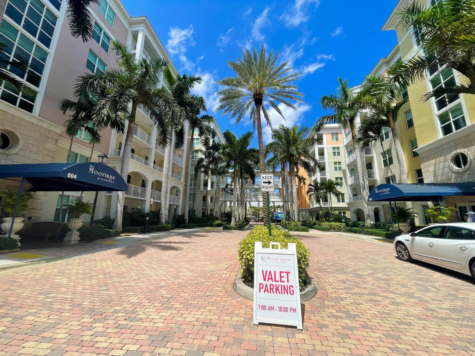 A brick-paved courtyard sits between two multi-story apartment buildings with palm trees and valet signage — 804 E Windward Way, Lantana FL 33462, LANTANA, FL