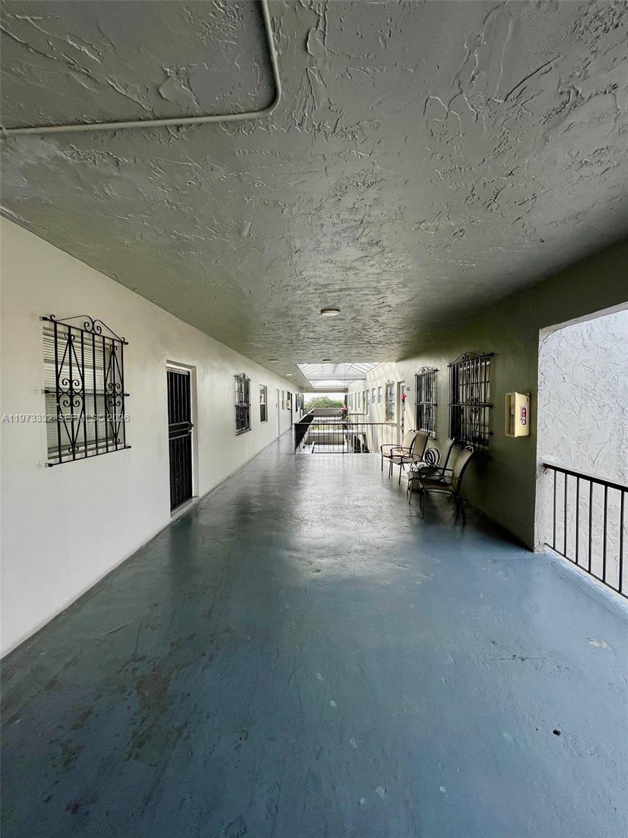 An outdoor apartment building walkway features a painted concrete floor and metal security window grilles — 1035 W 77th St # 412, Hialeah FL 33014, HIALEAH, FL