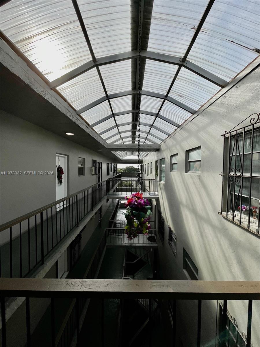 An open-air apartment building corridor features a translucent roof and metal railings — 1035 W 77th St # 412, Hialeah FL 33014, HIALEAH, FL