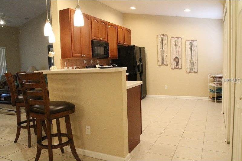 A kitchen with wood cabinets, black appliances, a breakfast bar, and tile flooring — 6453 ALCALDE CT UNIT 104, ORLANDO, FL