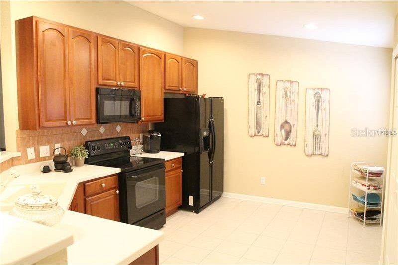 A kitchen with wood cabinets, black appliances, and three framed utensil art pieces on the wall — 6453 ALCALDE CT UNIT 104, ORLANDO, FL