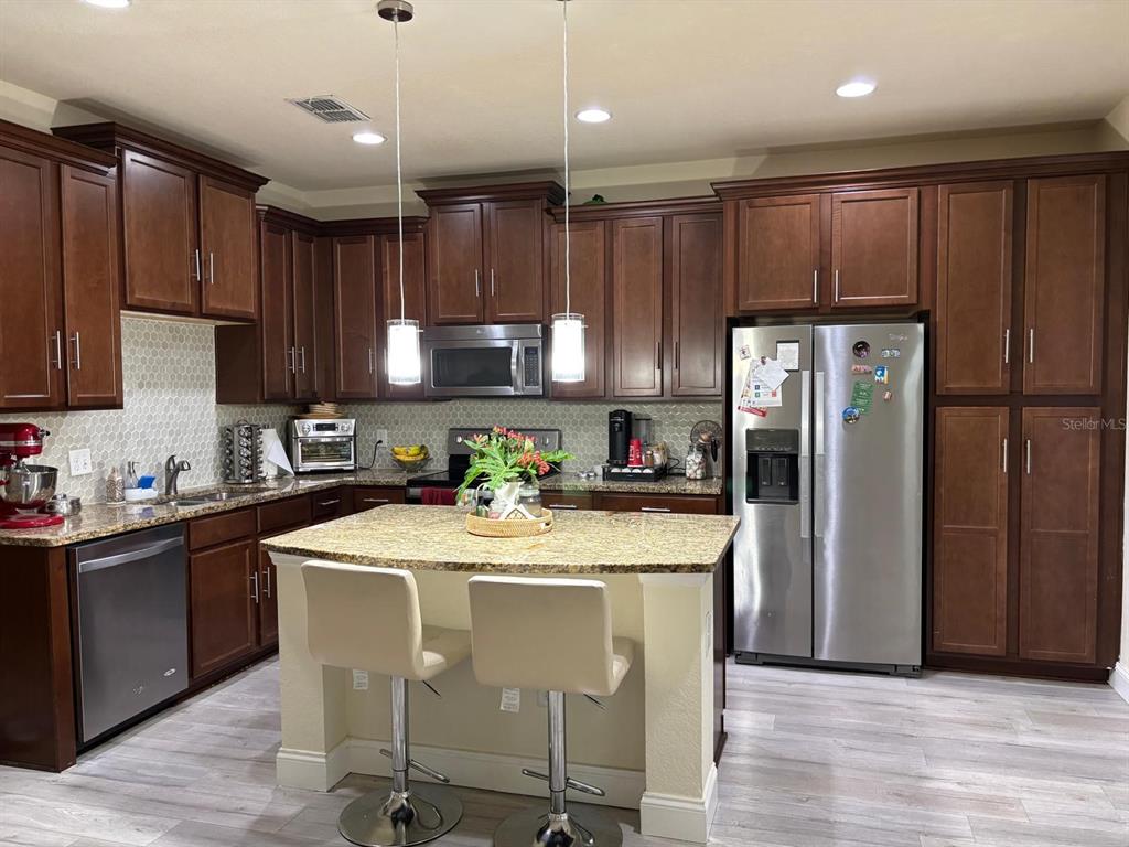 A kitchen features dark wood cabinets, granite countertops, a central island, and stainless steel appliances — 10108 EAGLE CREEK CENTER BOULEVARD, ORLANDO, FL