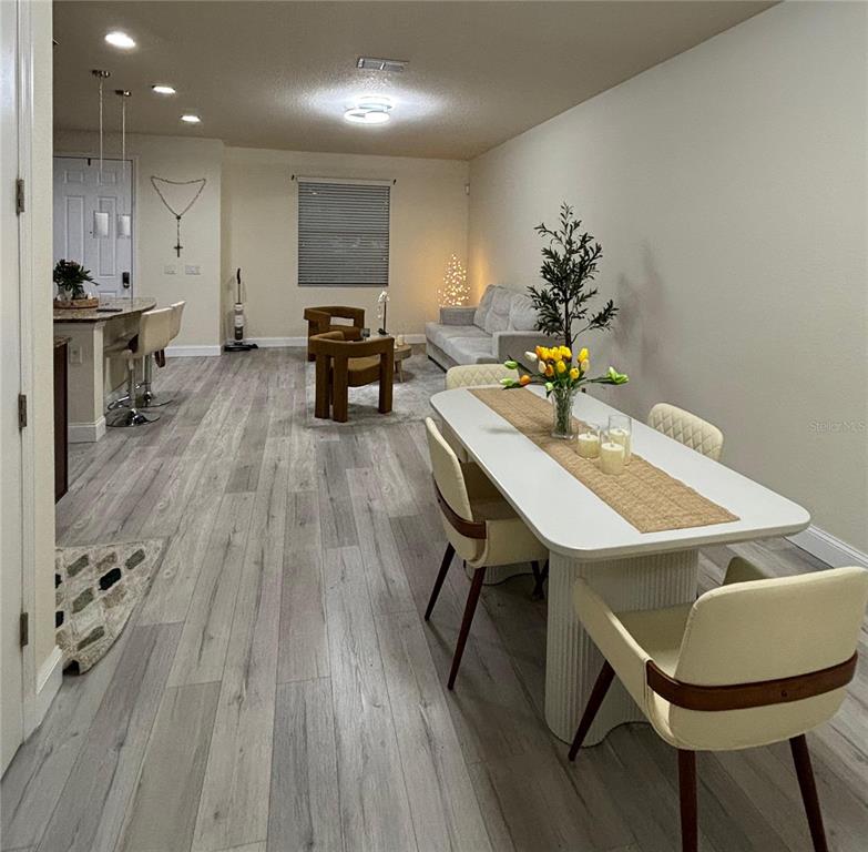 An open-concept living and dining area features light wood-look flooring and modern furniture — 10108 EAGLE CREEK CENTER BOULEVARD, ORLANDO, FL