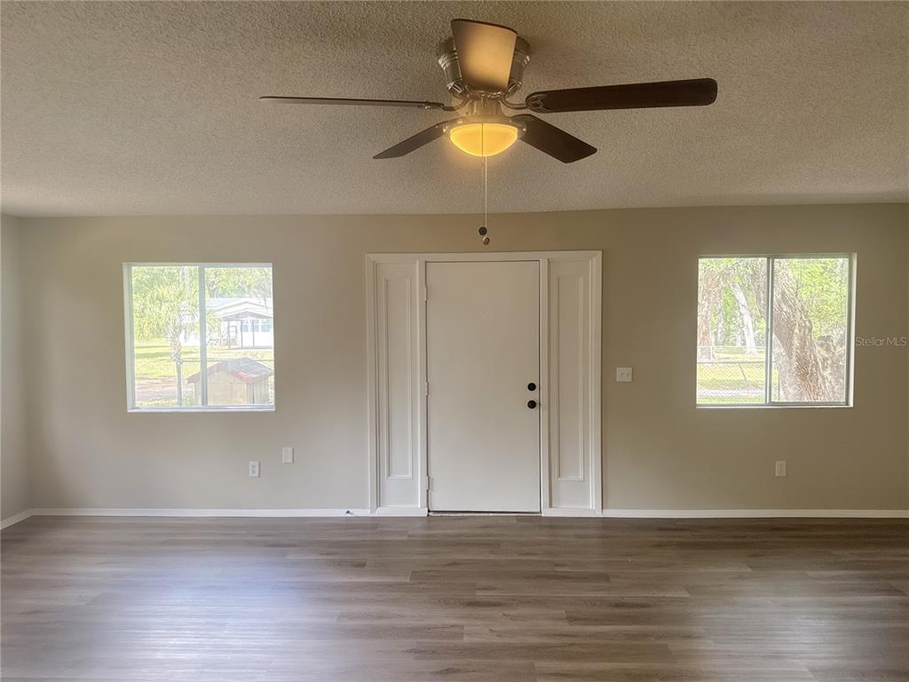 A living room features light gray walls, wood-look flooring, a ceiling fan, and a front door — 11345 SE 188TH AVENUE, OCKLAWAHA, FL