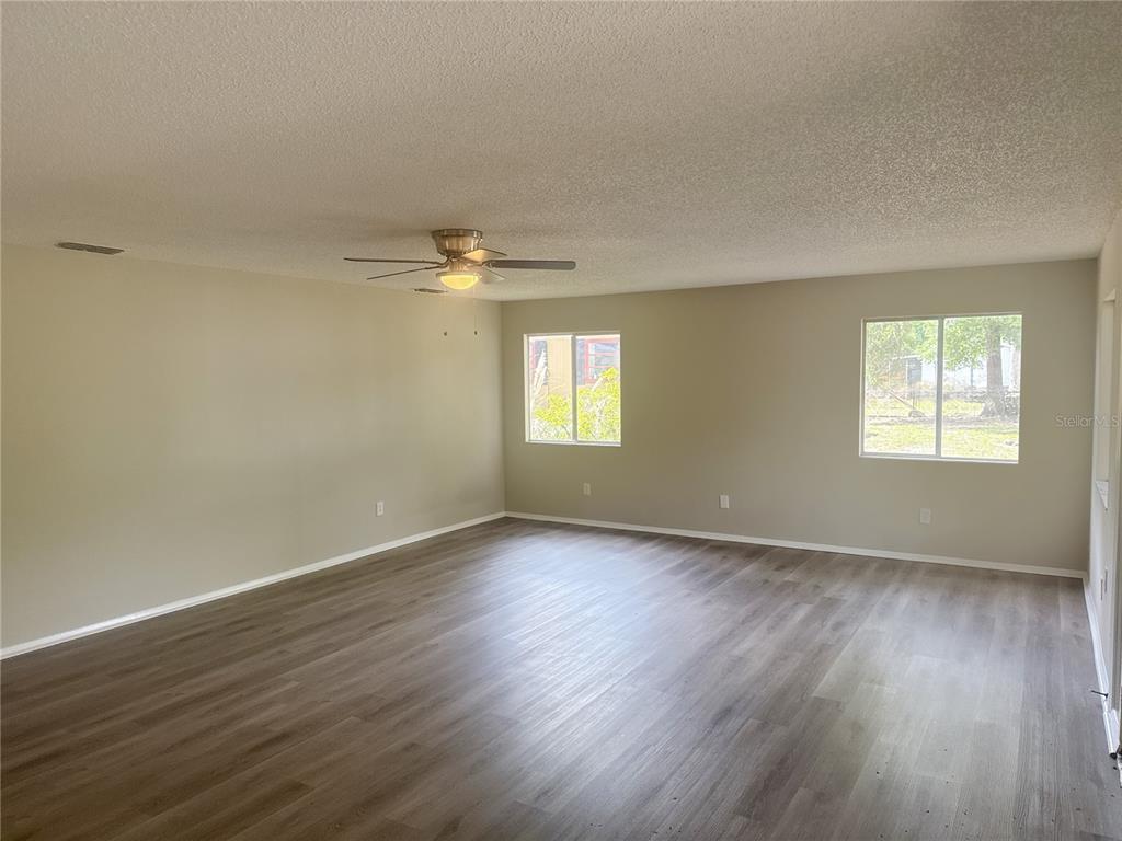 An empty living room features light-colored walls, wood-look flooring, a ceiling fan, and two windows — 11345 SE 188TH AVENUE, OCKLAWAHA, FL
