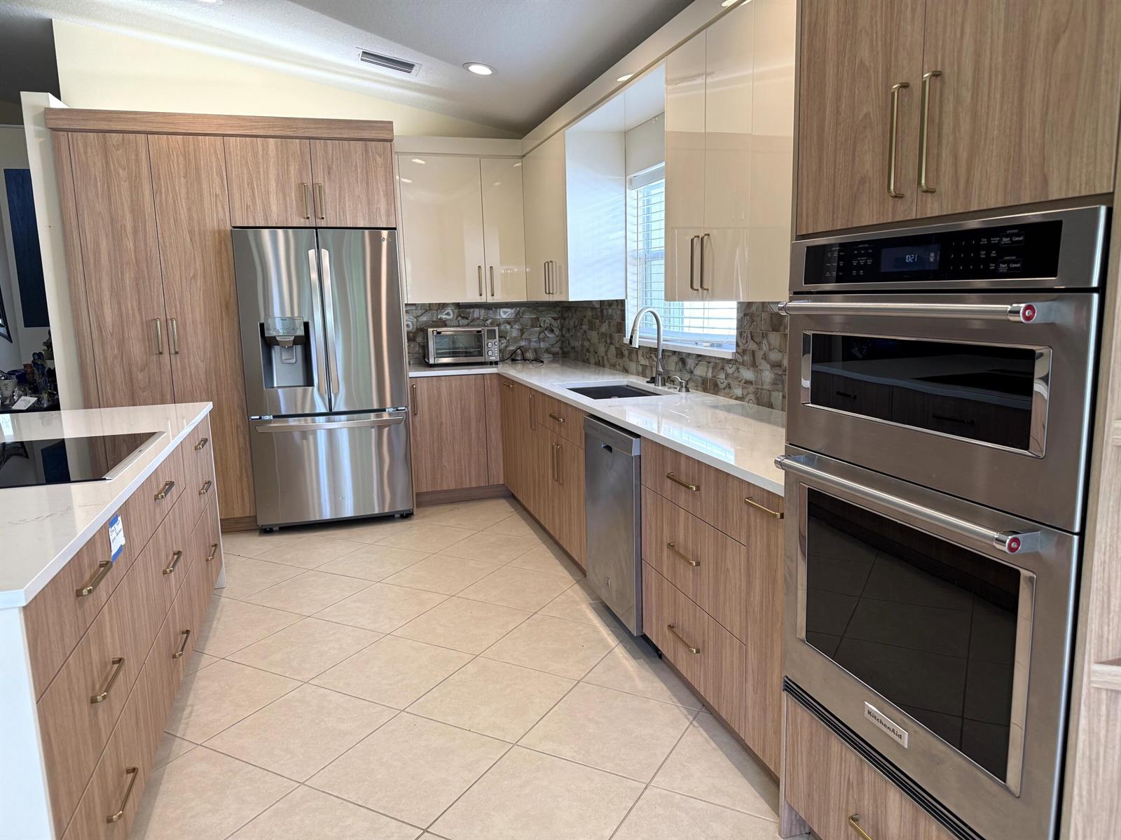 A modern kitchen features two-tone wood and white cabinets, stainless steel appliances, and tile flooring — 8135 Playa Del Sur Boulevard, Lake Worth FL 33467, LAKE WORTH, FL