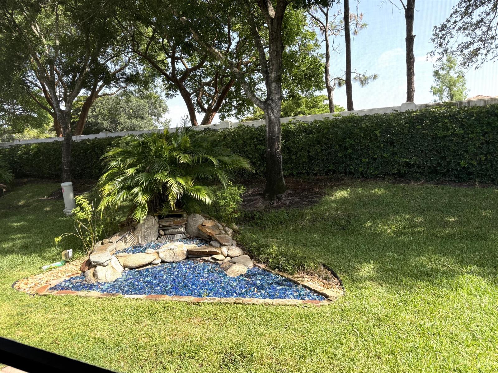 A backyard features a triangular garden bed filled with blue glass mulch and stone accents — 8135 Playa Del Sur Boulevard, Lake Worth FL 33467, LAKE WORTH, FL