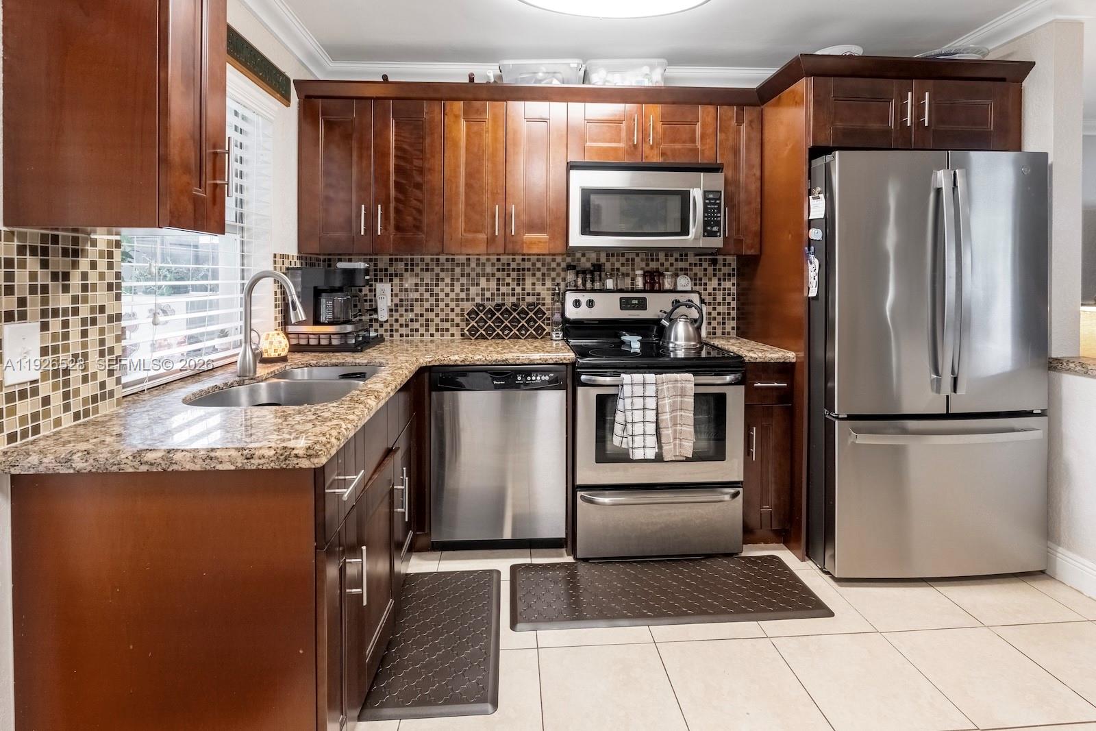 A kitchen features dark wood cabinets, stainless steel appliances, granite countertops, and a tiled backsplash — 7002 NW 95th Ave, Tamarac FL 33321, TAMARAC, FL