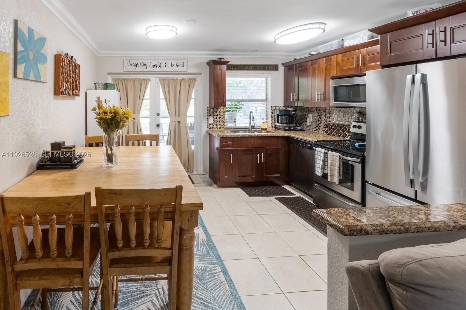 A kitchen and dining area features wooden cabinets, stainless steel appliances, and a wooden table — 7002 NW 95th Ave, Tamarac FL 33321, TAMARAC, FL
