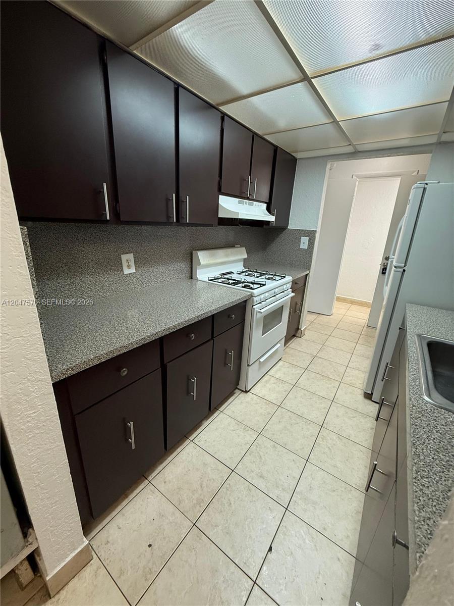 A galley kitchen features dark brown cabinets, speckled countertops, and white appliances — 1305 W 53rd St # 406, Hialeah FL 33012, HIALEAH, FL