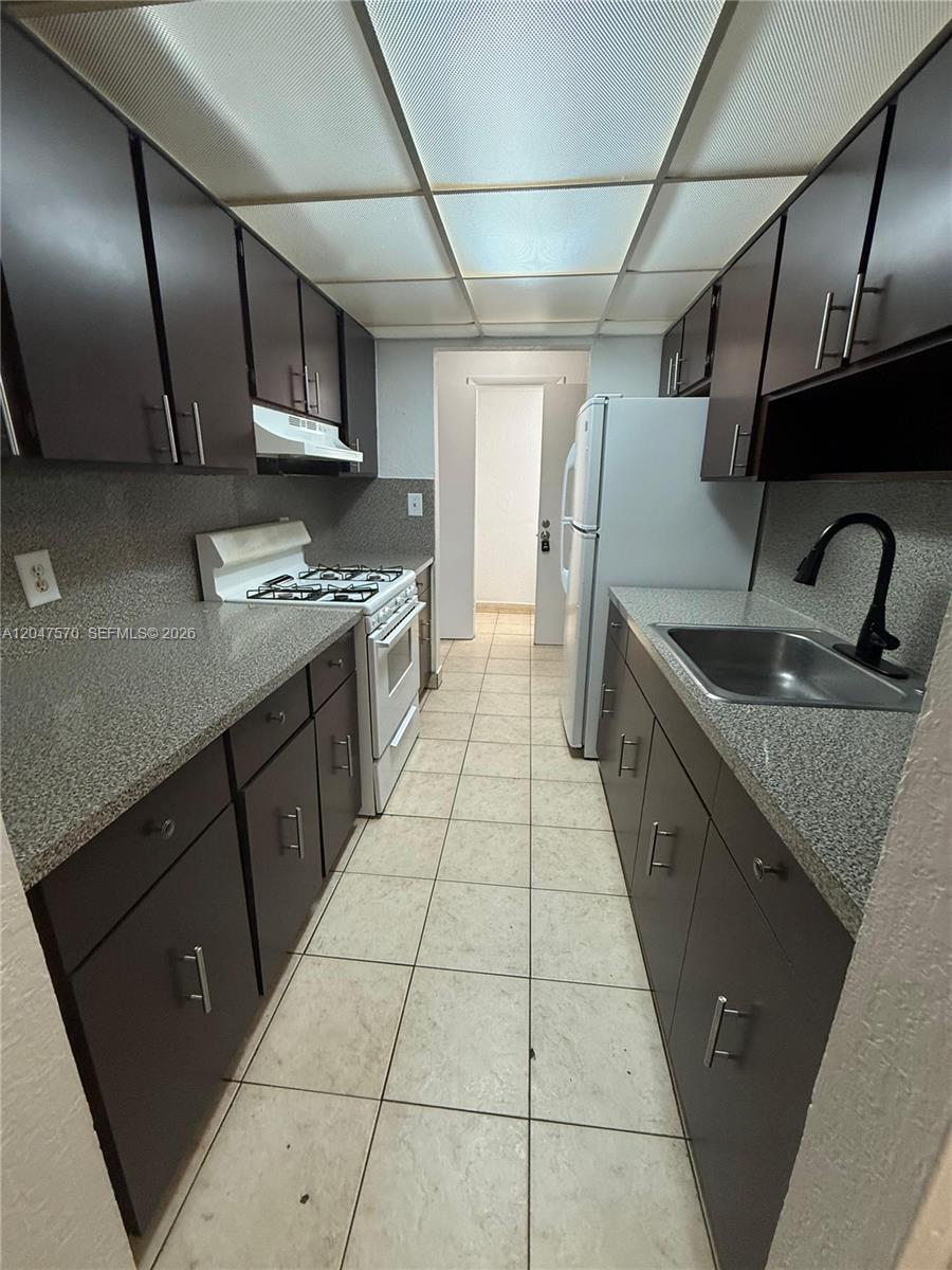 A galley kitchen features dark brown cabinets, speckled countertops, a gas stove, and tile flooring — 1305 W 53rd St # 406, Hialeah FL 33012, HIALEAH, FL